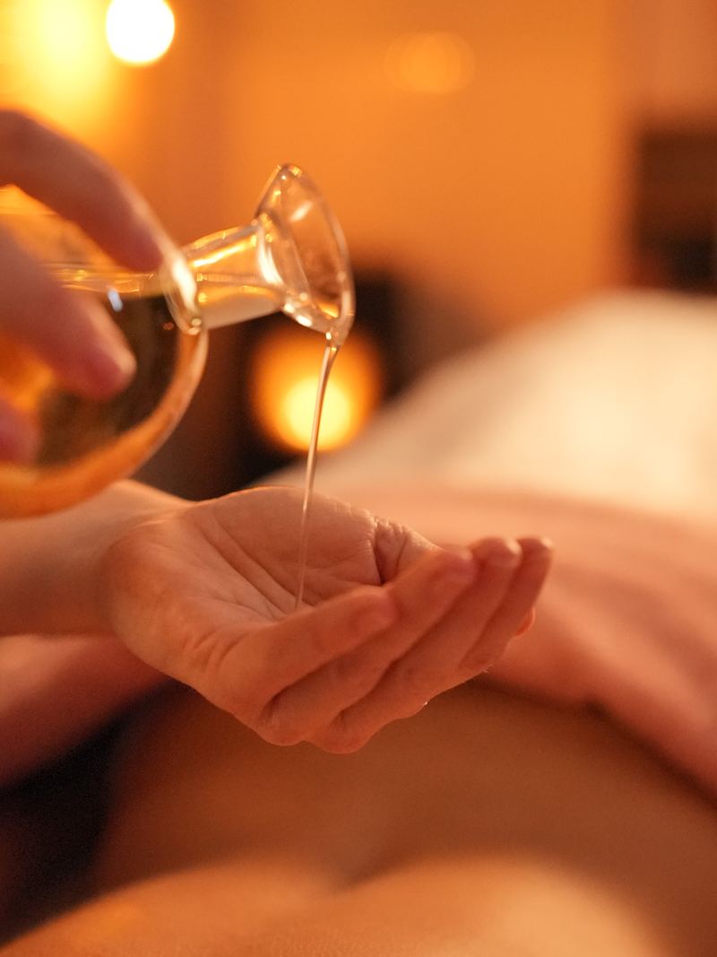 Massageolie wordt uit een glazen karaf in een open hand gegoten, in warm kaarslicht