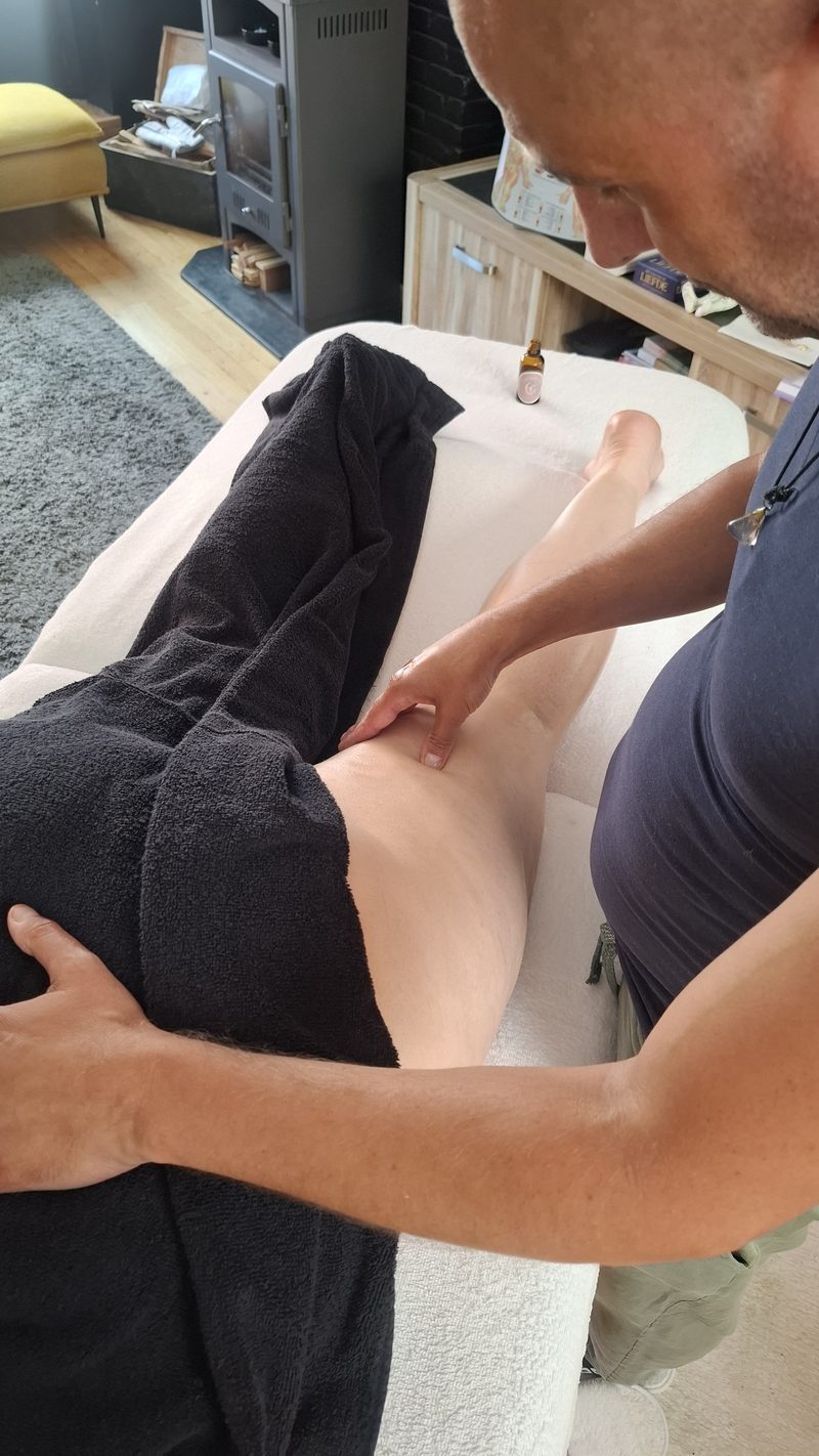 Handen werken op de benen van iemand die op de massagetafel ligt