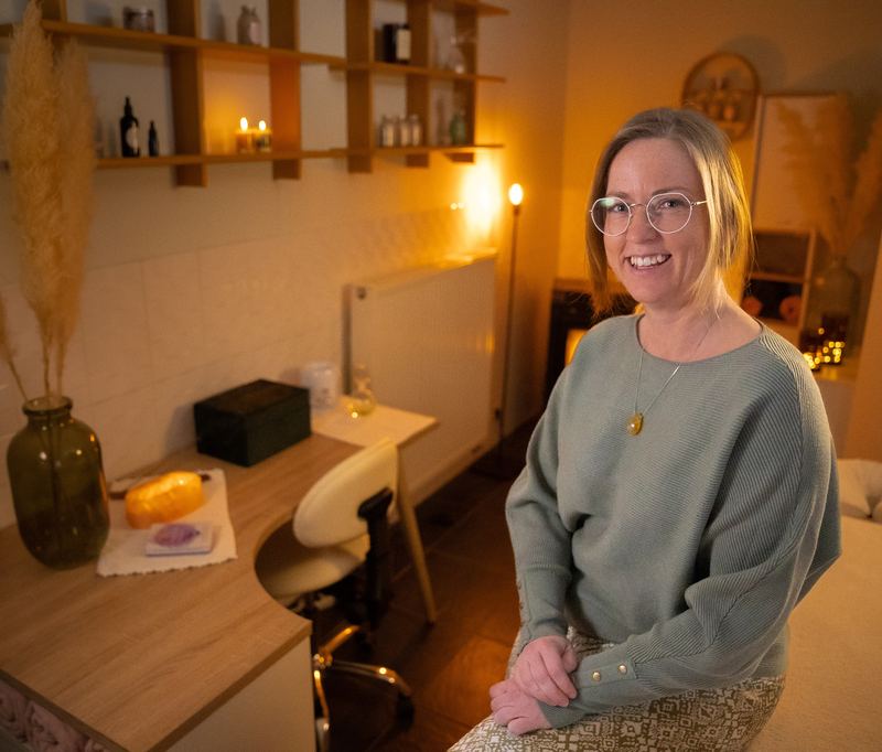 Lesley staat glimlachend in haar warm verlichte praktijkruimte